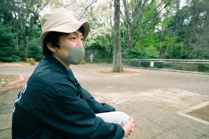 Man with beige hat and gray facemask sitting at a park