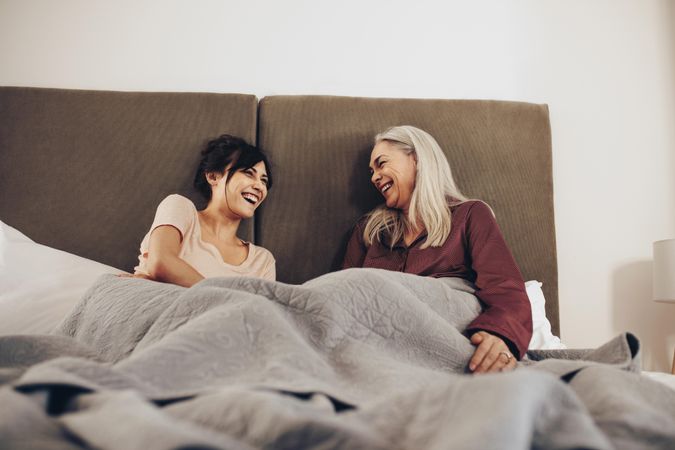 Mature woman sitting on bed with her adult daughter and laughing
