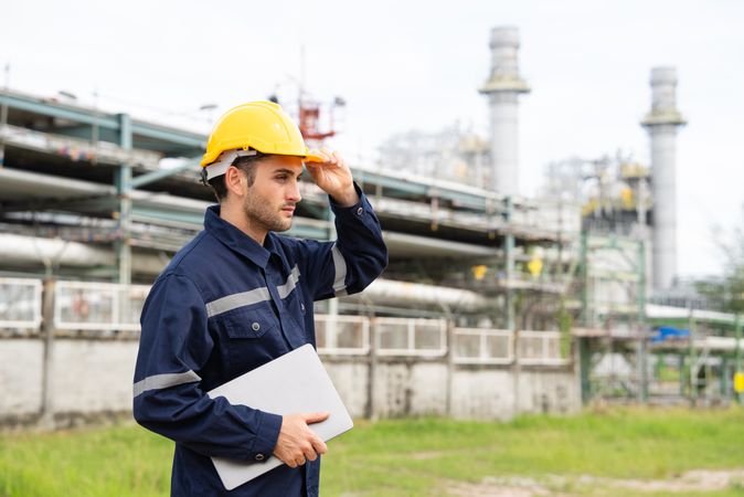 Refinery oil engineer worker in protection hardhat with laptop inspecting at petrochemical factory.