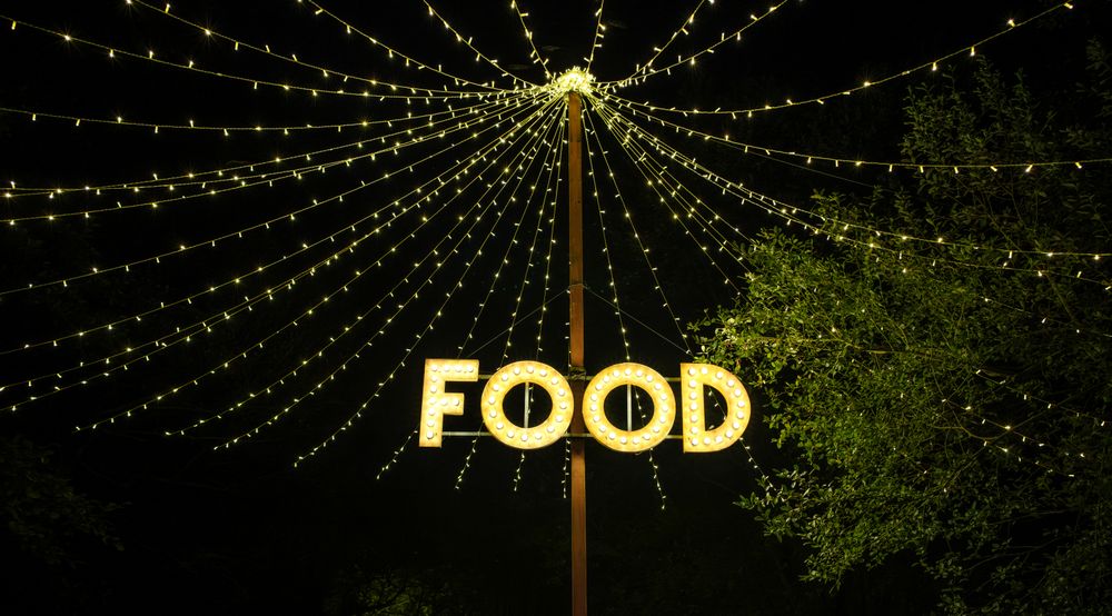 Signboard with word food made with light bulbs hung on wooden post under light garlands