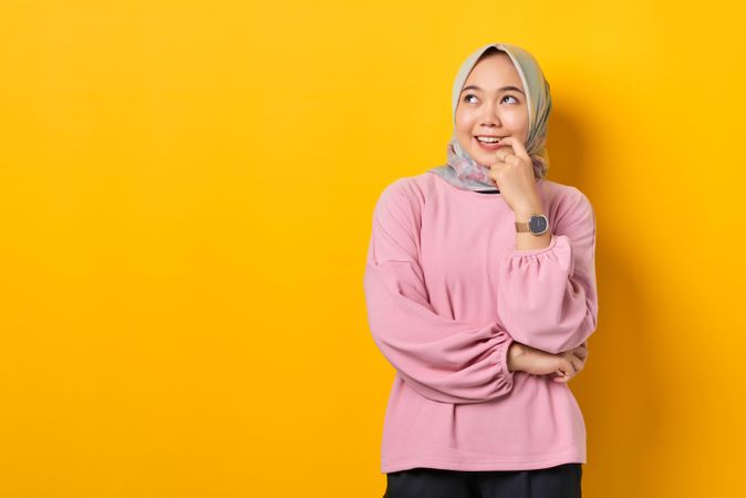 Muslim woman in headscarf thinking with anticipation about something with hand on chin