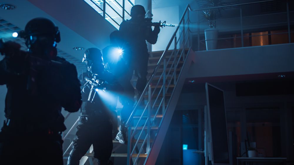 Masked Squad of Armed SWAT Police Officers Run Down the Stairs from a Second Floor in a Dark Office Building.