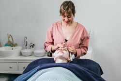 Crop beautician cleansing face of woman in salon