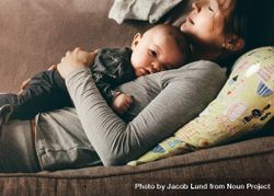 Mother taking rest sleeping on a couch with her baby on her chest 0LN3E4