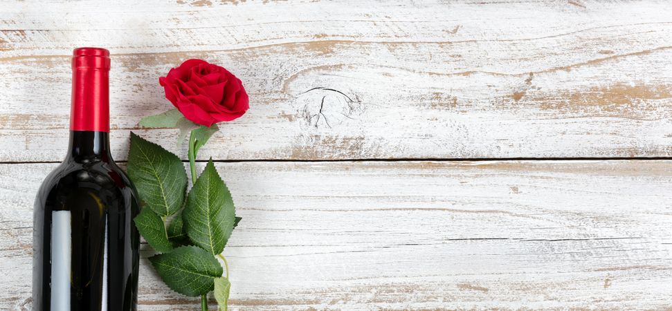Valentine’s Day celebration with red wine and a single rose on rustic wooden background