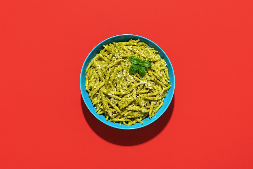 Pasta with pesto sauce, top view on a red background