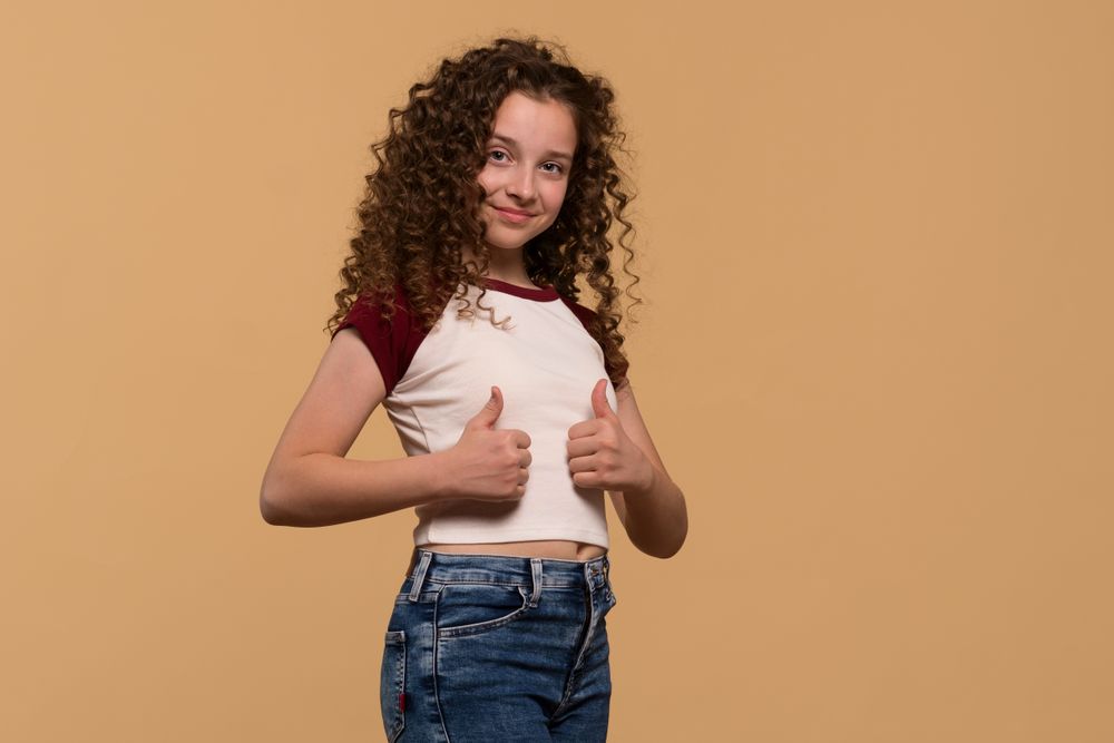 Young girl showing thumbs-up pose, smiling confidently