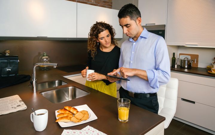 Couple looking at news on tablet while having quick coffee in home before work