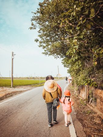 Person and child walking on road near trees