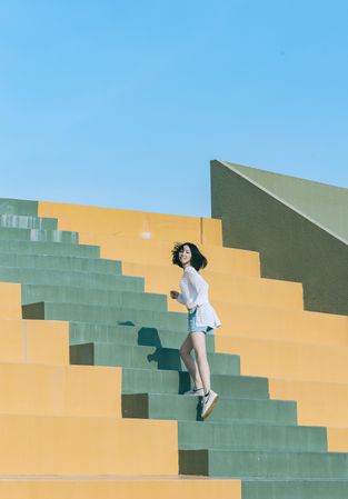 East Asian woman climbing yellow and orange staircase in sparse outdoor