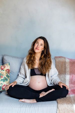 Pregnant woman deep in thought while sitting cross legged on sofa