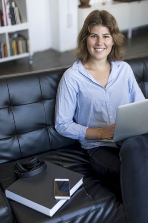 Smiling woman sitting on a sofa at home working on a laptop