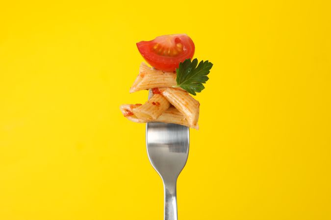 Fork with tasty pasta on yellow background, close up