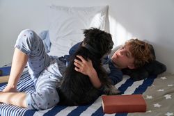 Calm boy lying with dog on bed