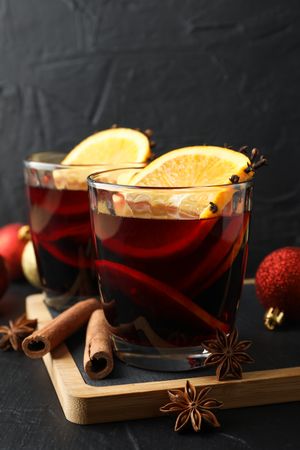 Glasses of tasty mulled wine and christmas baubles on dark background, space for text
