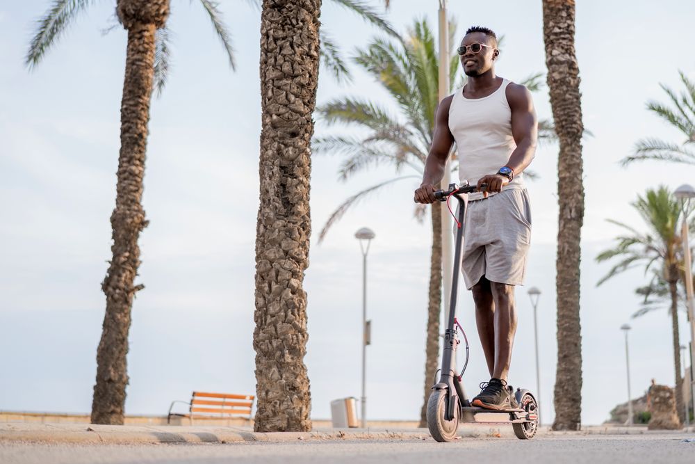 Cool adult Black man riding scooter in street