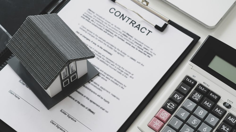 Model house put on contract documents with calculator and laptop