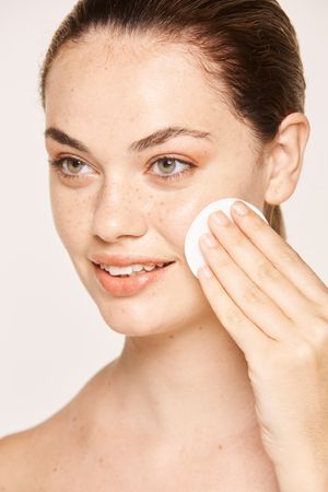Peaceful female applying toner on radiant face with sponge