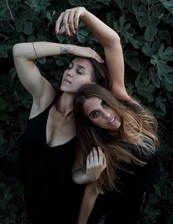 Young women posing near green bush
