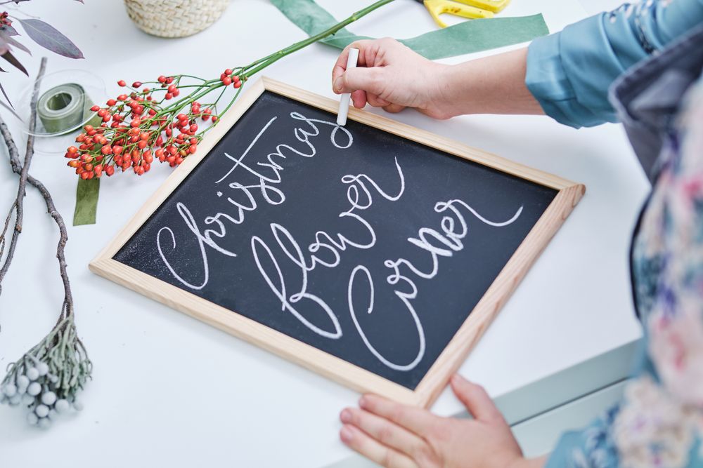 Crop woman writing on board with chalk in flower store