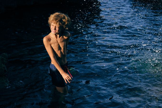 Boy grimacing in wavy sea with splashing water
