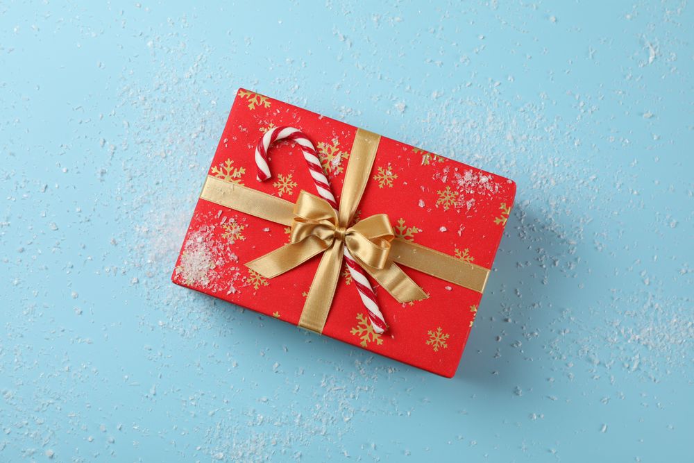 Gift box, candy cane and snow on blue background, top view