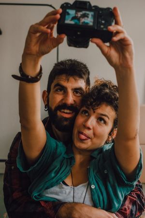Joyful couple embracing and taking selfie on camera at home