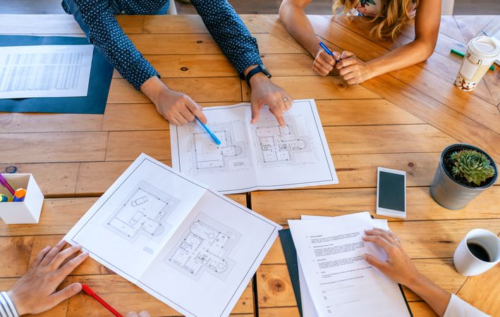 Top view of unrecognizable architects in a work meeting looking at construction plans
