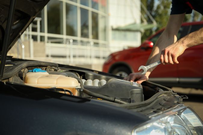 A man holds a wrench over a car engine. Car inspection
