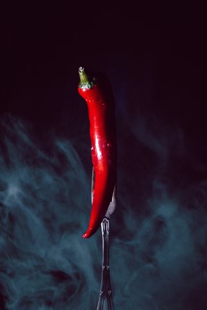 red chili pepper in fork on a dark background with smoke