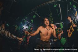 Sweaty long-haired shirtless male musician grabs microphone on stage during concert 4BaAk5