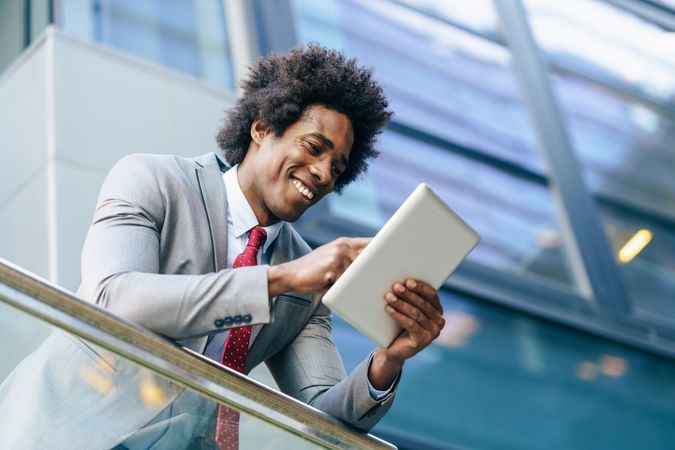 Happy man leaning on banister looking at digital tablet