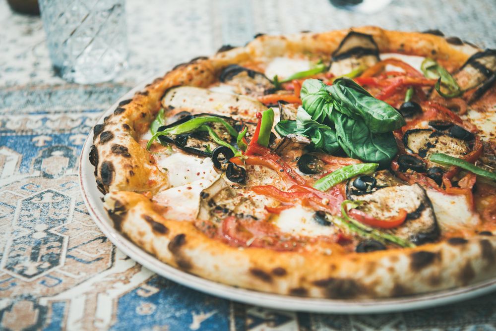 Wood fire vegetable pizza on tiled table with crystal glass