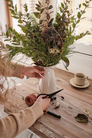 Crop florist preparing composition of green branches on table