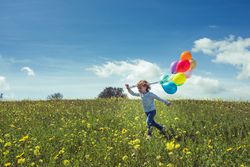 Positive boy with balloons enjoying summer in green field