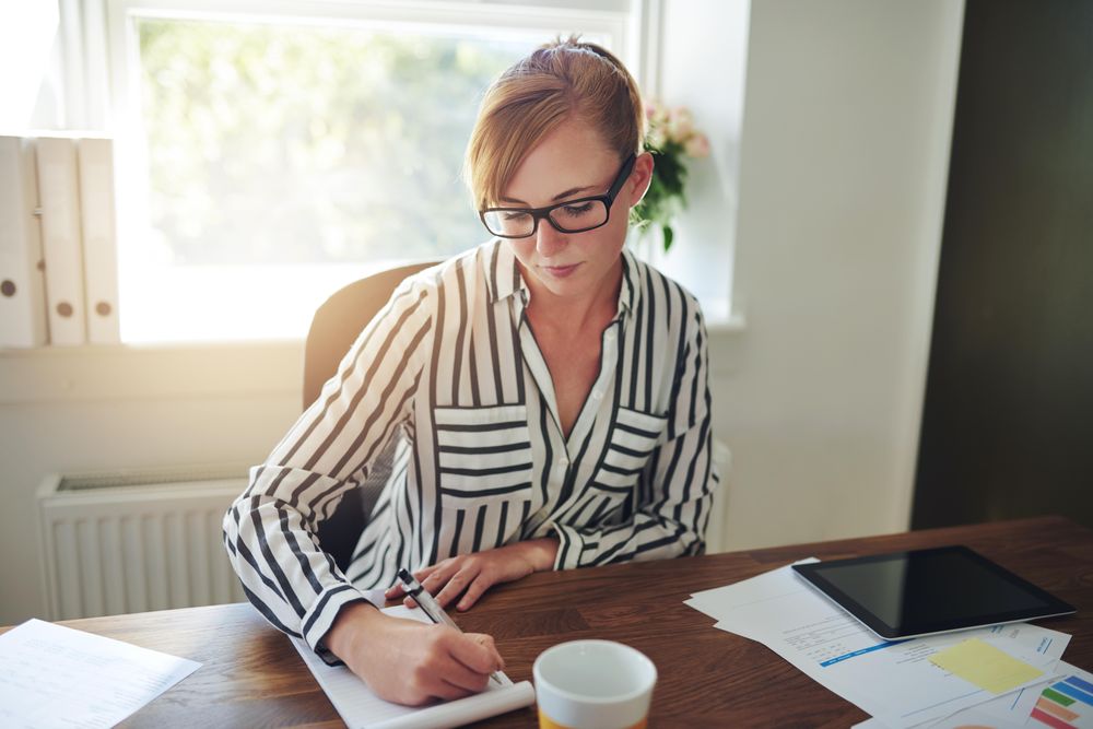 Woman in striped shirt taking notes at her desk