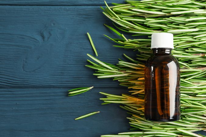 Rosemary oil and leaves on wooden background, space for text