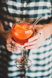 Young woman in checkered dress holding aperitif with orange slices and glass straw