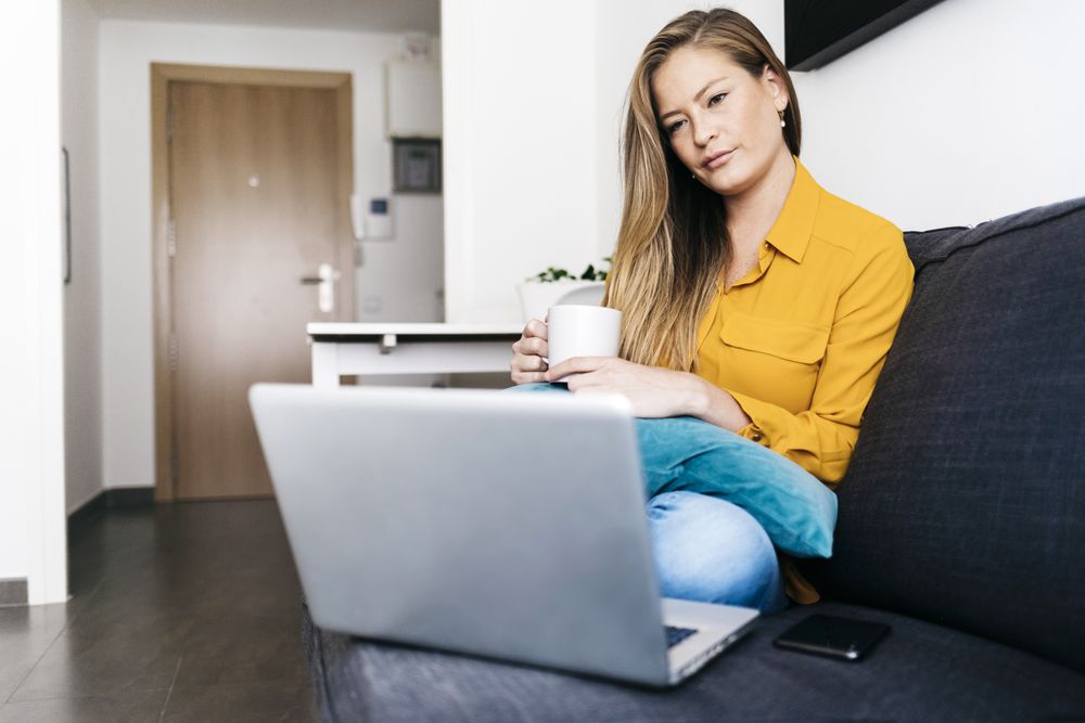 Long haired female sitting on sofa with laptop computer working remotely from home