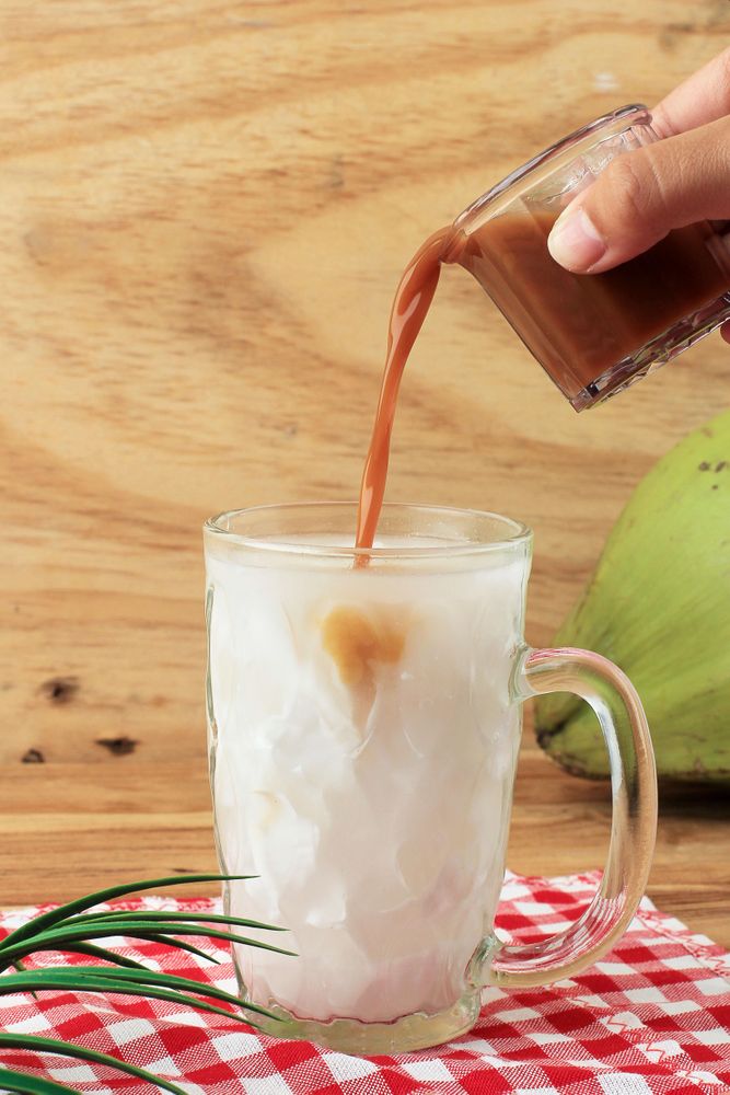 Hand pouring syrup into iced mug on table
