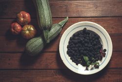 Ripe blackberries garnished by vegetables in bowl on wooden background