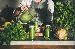 Woman pouring green smoothie from blender into jars in kitchen