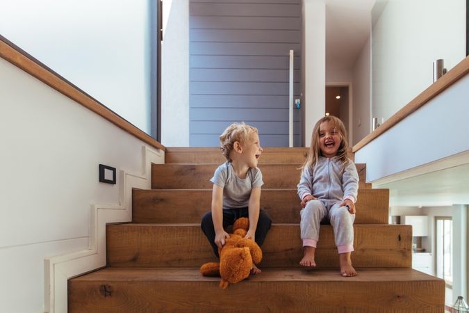 Laughing little boy and girl sitting on wooden stairs with teddy bear