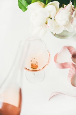 Bottle in foreground pouring glass of pink rose wine, and bottle with flowers