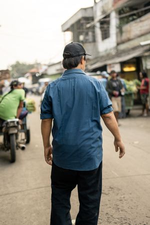 Back view of man in blue shirt and dark pants standing on street