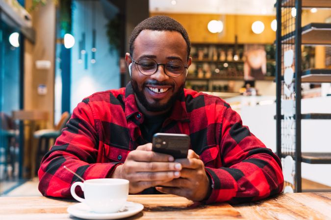 Cheerful Black man with smartphone in cafe