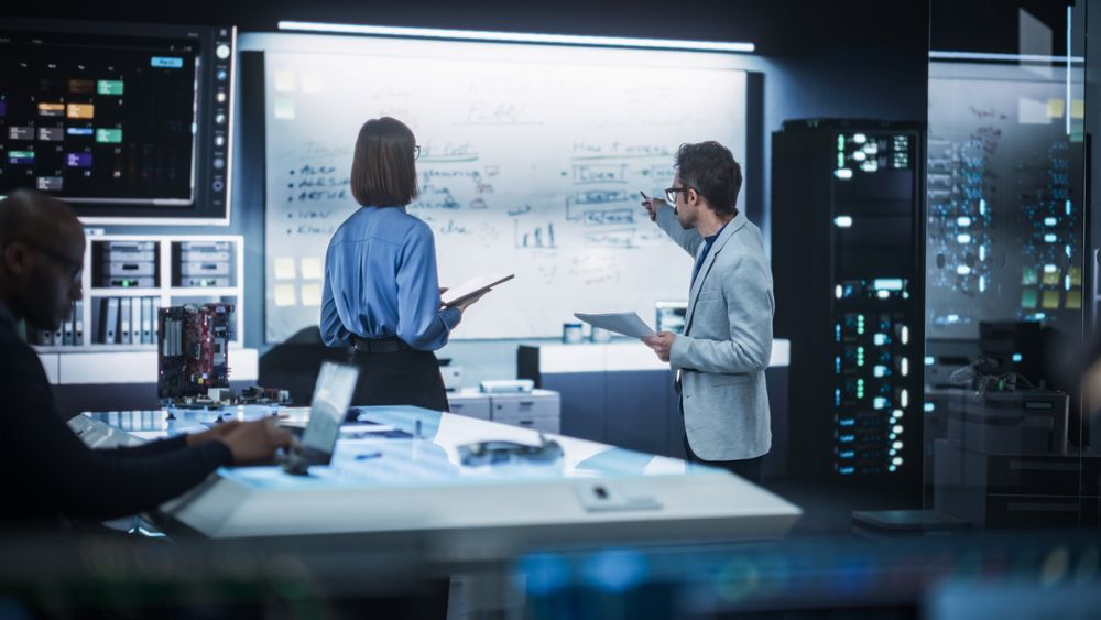 In Technological Research Facility: Portrait of a Team of Two Professional Engineers Using Digital Tablet and White Board to Discuss the Manufacturing Plan for Product Development