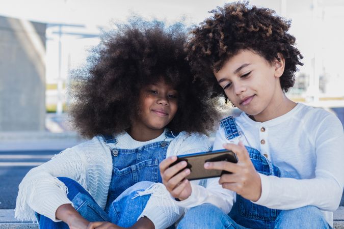 Black kids using smartphone together on street