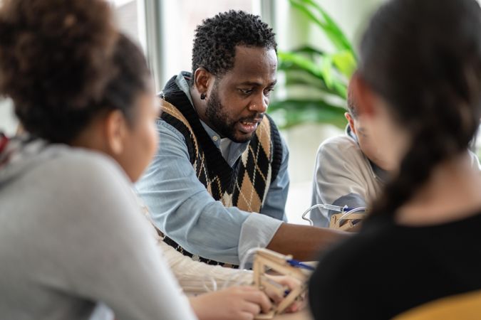Black male teacher speaking to teenager students around a table
