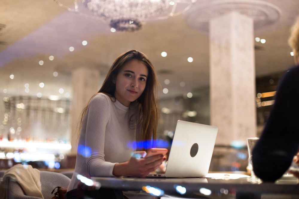 Serious young woman texting in a cafe with laptop in front of her